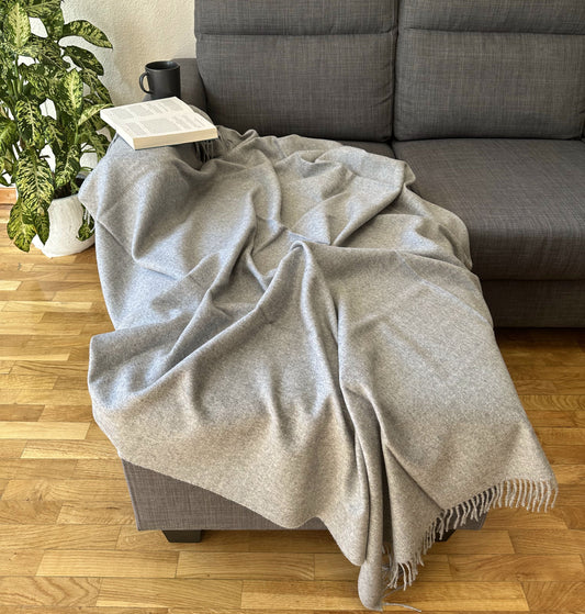 Soft grey alpaca throw used on bed and sofa, combining warmth, style, and comfort for a cozy and refined home atmosphere.
