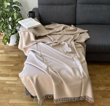 Luxurious beige alpaca blanket draped on a sofa, perfect as a cozy throw for bed or living room.
