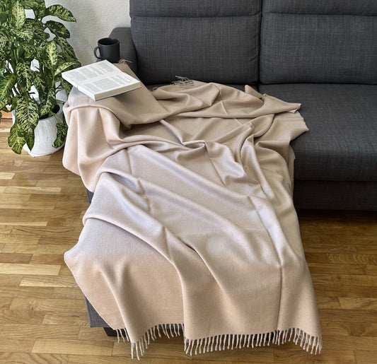 Luxurious beige alpaca blanket draped on a sofa, perfect as a cozy throw for bed or living room.